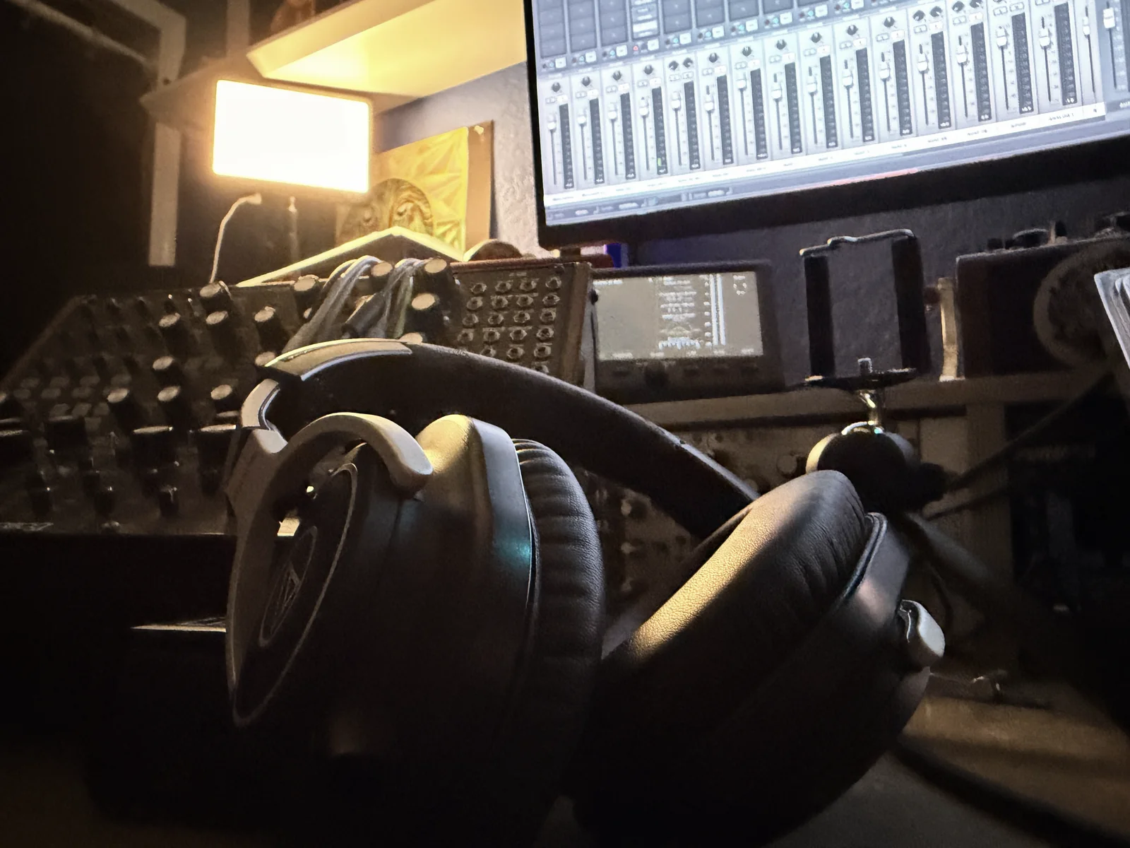 Headphones resting on the studio desk in warm light, synths and a mixer behind
